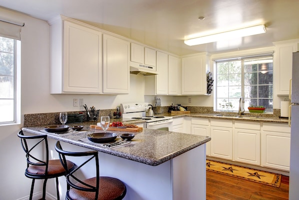 Una cocina con armarios blancos, encimeras de granito y una isla central con taburetes de bar.