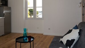 A modern living room with a grey sofa, a small black table with a blue vase and a red cup, and a magazine on the sofa.
