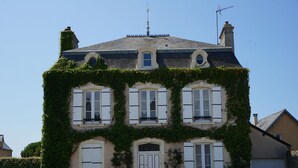A two-story building with a steeply pitched roof, white shutters, and a small balcony.