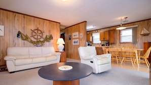 A living room with a round coffee table, a sofa, a chair, and a dining area with wooden chairs and a table.