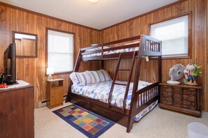 Une chambre avec un lit superposé, des murs en bois, un petit bureau, un miroir et un ventilateur.