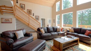 Ein geräumiges Wohnzimmer mit Ledersofas, einem Holztisch und einer Treppe mit Holzhandläufen.