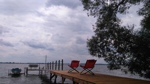 A wooden dock extending into a body of water with two red chairs and a bench.