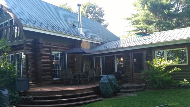 A log cabin with a covered patio, outdoor seating, and a metal roof.