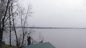 A small cabin with a green roof, a wooden deck, and a view of a large body of water.