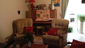 Een woonkamer met twee fauteuils, een salontafel, een lamp, een schilderij en een raam met gordijnen.