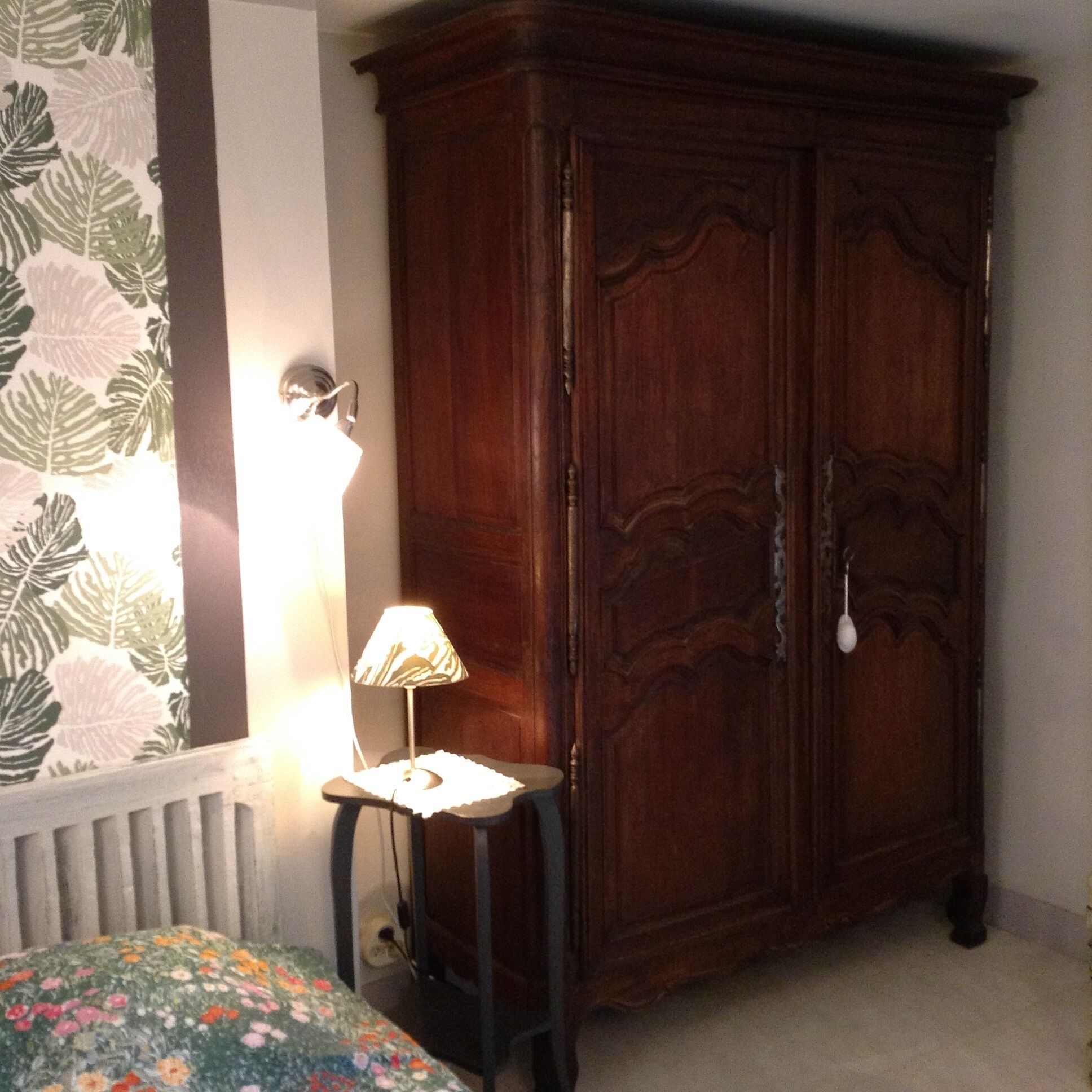 A bedroom with a wooden wardrobe, a bedside table with a lamp, and a floral bedspread.