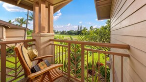 A wooden deck with a chair and a straw hat, overlooking a lush green landscape with palm trees.