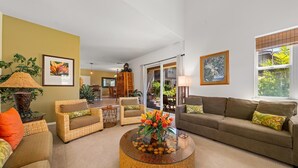 A living room with a round glass coffee table, wicker chairs, a sofa, and a dining area in the background.