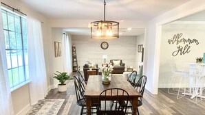 A spacious dining area with a wooden table and chairs, a hanging light fixture, and a view into the living room. - Bright, Spacious, Family-Friendly, 8 Blocks to Main St (Fredericksburg)