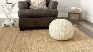 A living room with a dark leather sofa, a round woven ottoman, a wooden side table with a lamp, a clock on the wall, and a crate labeled "locally harvested honey." - Bright, Spacious, Family-Friendly, 8 Blocks to Main St (Fredericksburg)