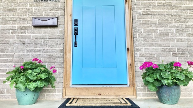 A blue door with a mailbox above it, a wooden door frame, and two potted plants with pink flowers on either side. - Bright, Spacious, Family-Friendly, 8 Blocks to Main St (Fredericksburg)
