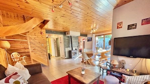 A spacious living room with a wooden ceiling, a large flat-screen TV, a red rug, and a staircase leading to another level. - CHALET "Les roses de Jean" 2 to 10 people (VENOSC)