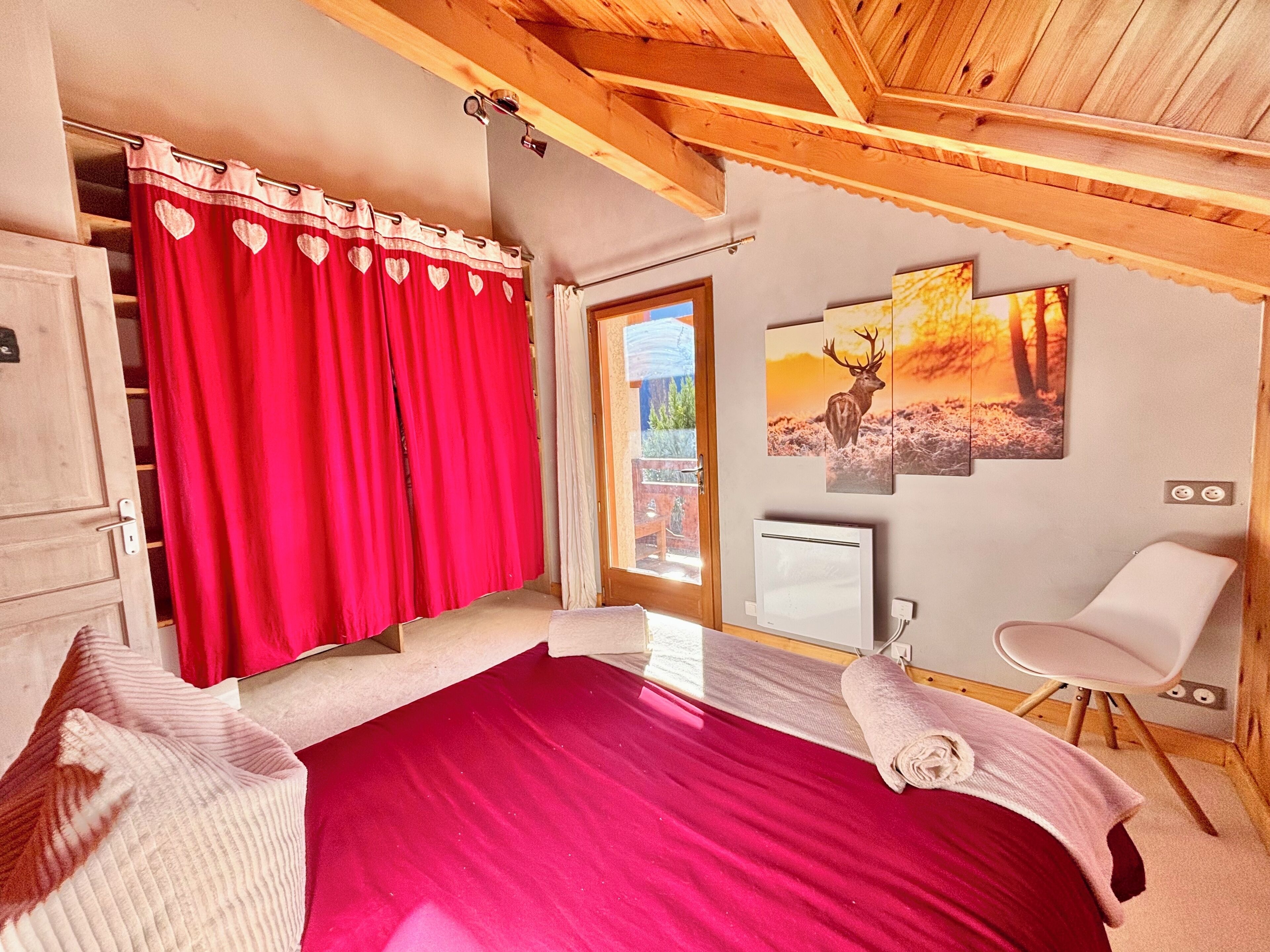 Een slaapkamer met een bed, een rood gordijn, een witte stoel en een muur met een herten schilderij.