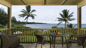 A covered outdoor area with wicker furniture and a view of the ocean.