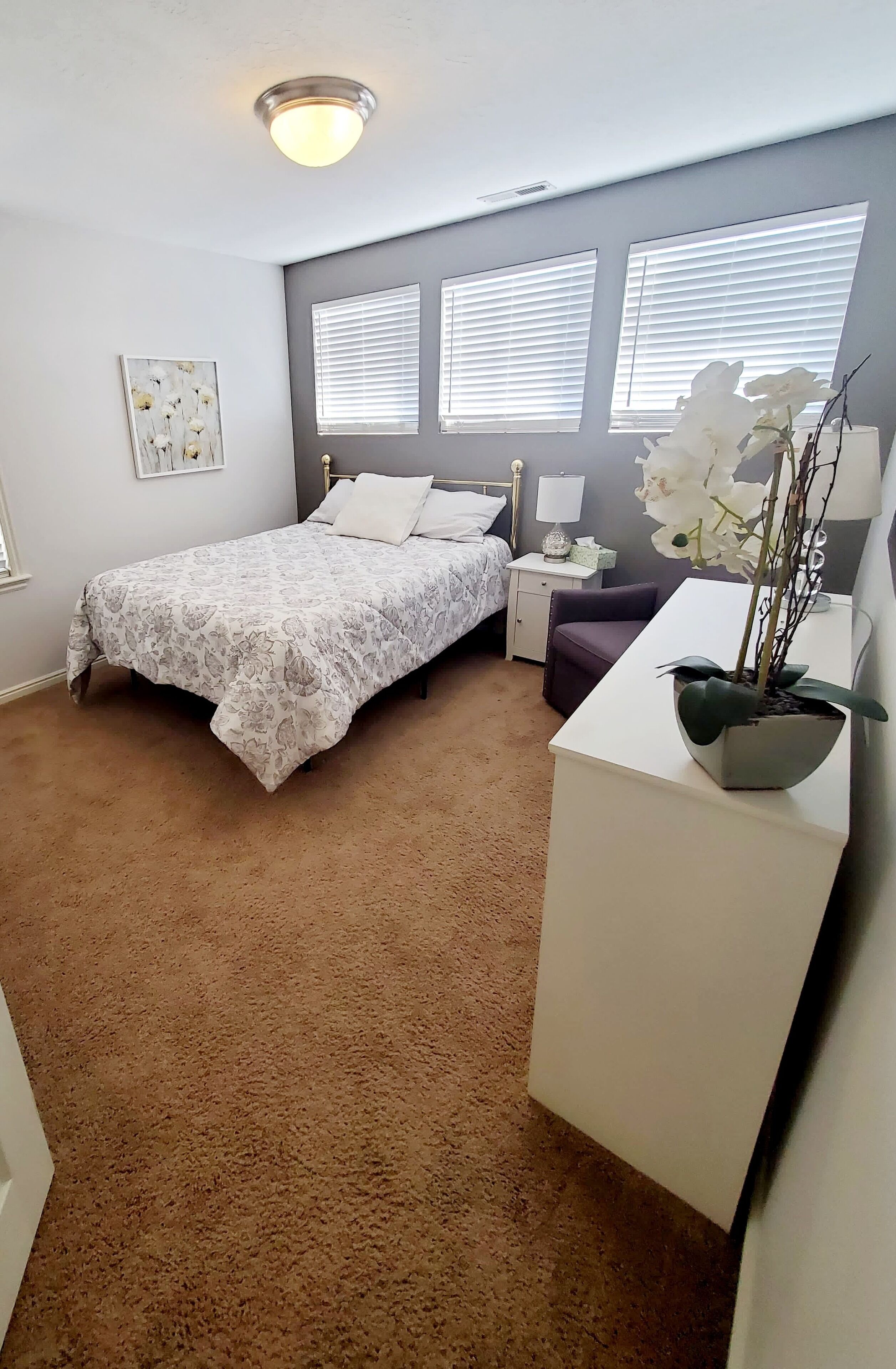 A bedroom with a bed, bedside table, lamp, and a potted plant.