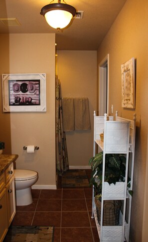 Une salle de bain avec des toilettes, un lavabo, une douche et une étagère sur laquelle est posée une plante.