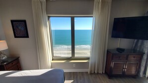A hotel room with a large window offering a view of the ocean. There is a bed, a dresser, and a television on the wall. - Royale Palms 1402 2 Br Oceanfront in Kingston,Pool (Myrtle Beach)