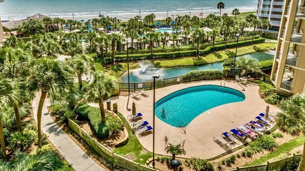 A resort with a large pool, palm trees, and a view of the beach. - Royale Palms 1402 2 Br Oceanfront in Kingston,Pool (Myrtle Beach)