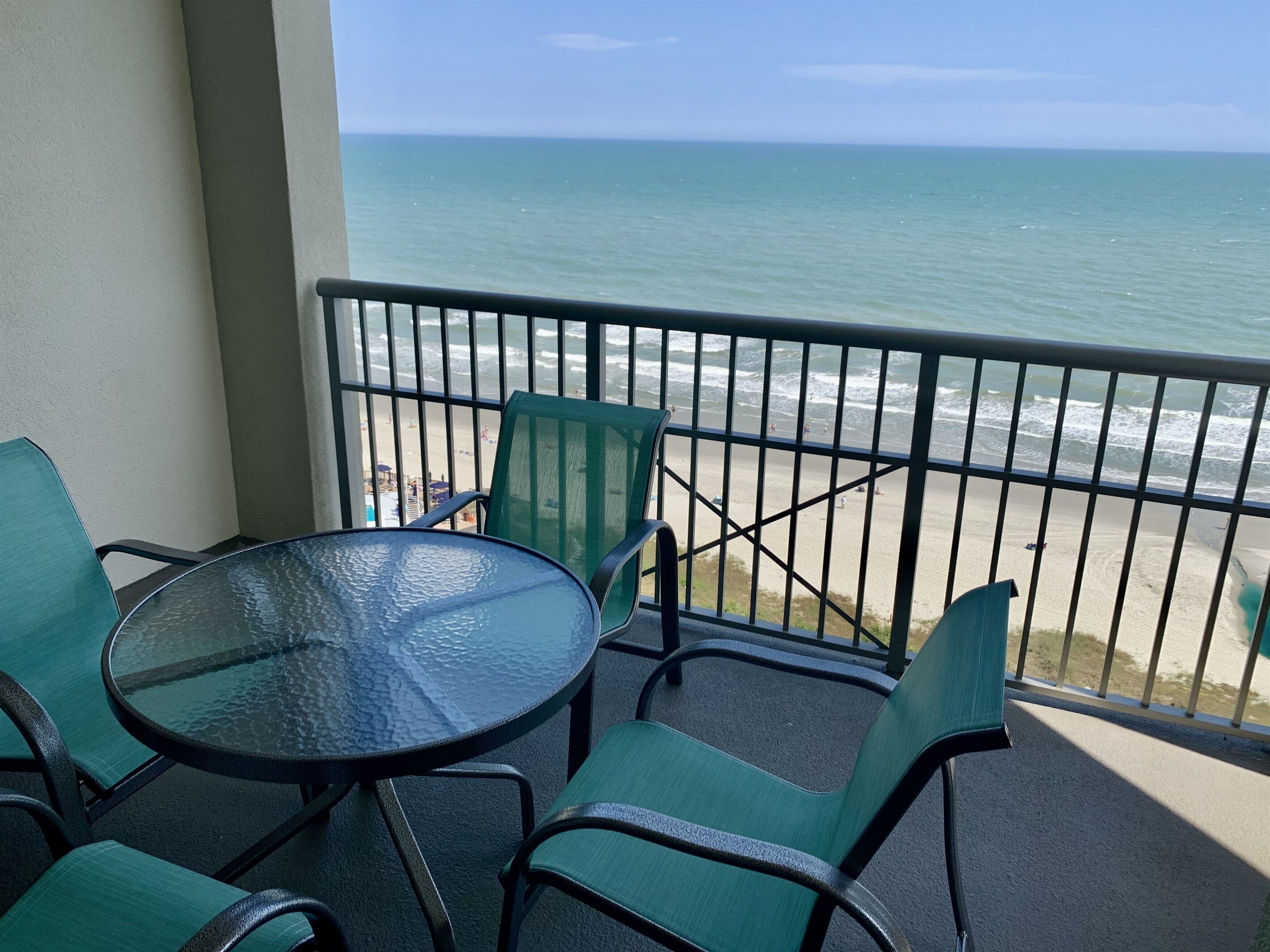 Varanda com mesa e cadeiras de vidro, com vista para uma praia e oceano.