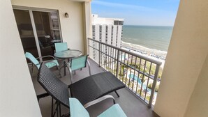 A balcony with a table and chairs, overlooking a beach and a high-rise building. - Royale Palms 1402 2 Br Oceanfront in Kingston,Pool (Myrtle Beach)