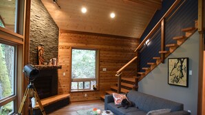 A cozy cabin interior with a stone fireplace, a wooden staircase, and a comfortable seating area. - Romantic island retreat  surrounded by majestic trees (Shelton)