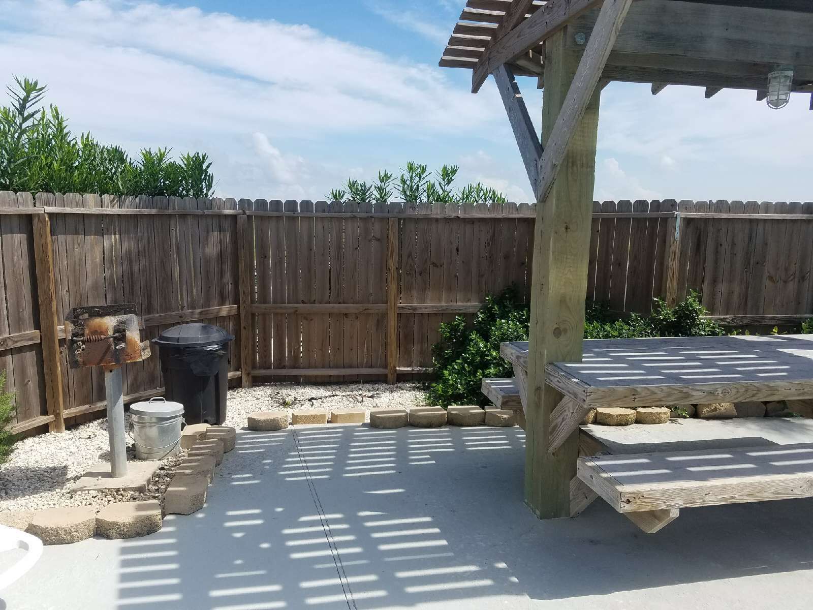 A wooden deck with a pergola, a barbecue grill, and a trash can.