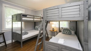 A bunk bed room with a ladder, a small table with a lamp, and a window with blinds.
