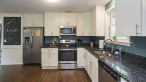 A modern kitchen with white cabinets, stainless steel appliances, a granite countertop, and a built-in dishwasher.