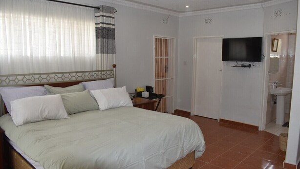 A hotel room with a large bed, a television mounted on the wall, a bathroom with a sink, and a window with curtains. - monavale hills getaway (Harare Central)