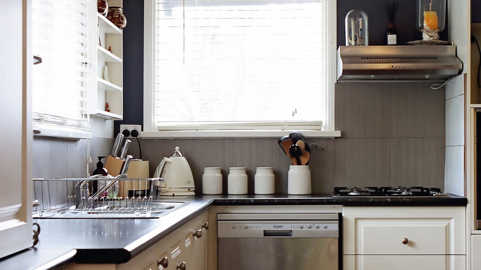 Une cuisine moderne équipée d’un lave-vaisselle, d’une cuisinière et d’une fenêtre avec des stores.