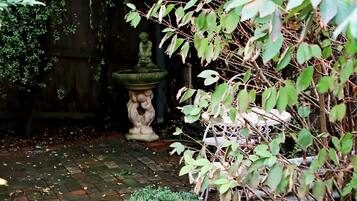 Een tuin met een stenen fontein, een beeld en een pad van baksteen.