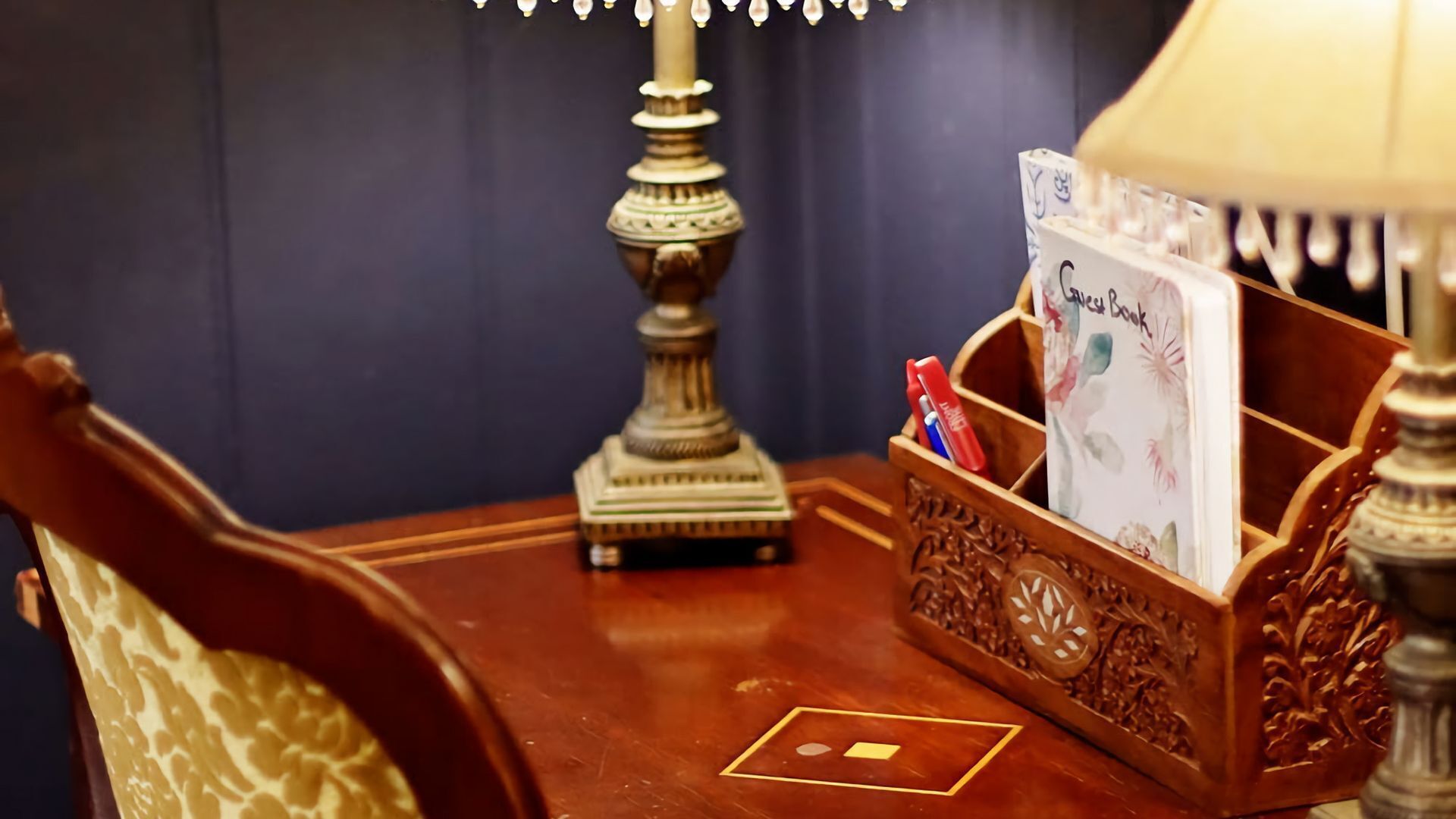 Et træsidebord med en lampe, en dekorativ æske og en kort holder med en bog med titlen "Guest Book".