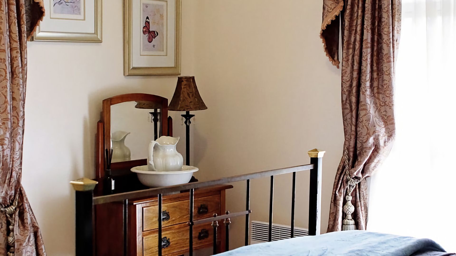 A bedroom with a wooden dresser, a mirror, a lamp, and a bed.