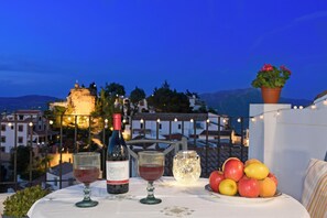 A table with a bottle of wine, two glasses, a decorative jar, and a plate of fruit on a balcony overlooking a cityscape at dusk. - Casa Bonita, an authentic Andalusian village experience. Pets-hispeed WIFI-airco (Comares)