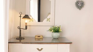 En vit byrå med en spegel, en liten vas med blommor och en lampa.