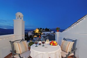 Una terraza con una mesa dispuesta para dos personas, que incluye una botella de vino, copas y un frutero.