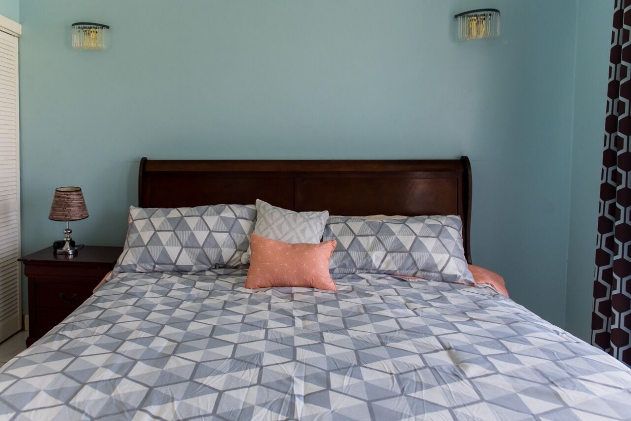 A bedroom with a bed, two wall-mounted lamps, a nightstand, and a patterned wall.