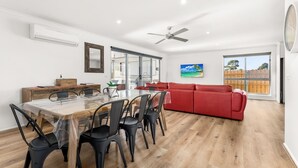 A spacious living area with a dining table, red sofa, and a ceiling fan. - Casa Killara - sleeps 14 (COWES)