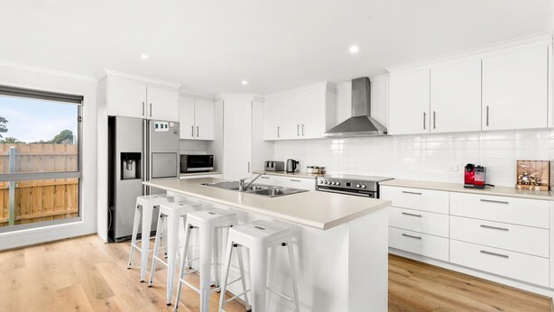 A modern kitchen with white cabinetry, a stainless steel refrigerator, a microwave, a stove, and a large island with bar stools. - Casa Killara - sleeps 14 (COWES)