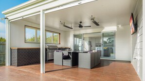 An outdoor patio with a barbecue, wicker furniture, ceiling fans, and a view of the backyard. - Casa Killara - sleeps 14 (COWES)