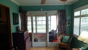 Quarto com cama, penteadeira, cadeira, janela com persianas e ventilador de teto.