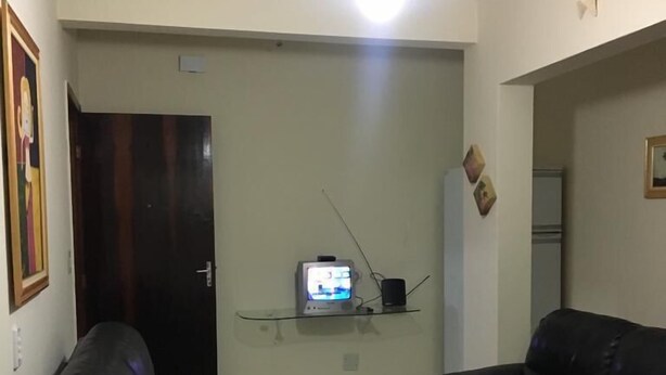 Ein Wohnzimmer mit zwei schwarzen Ledersofas, einem weißen Couchtisch, einem Fernseher auf einer Glasablage und einer Tür im Hintergrund.