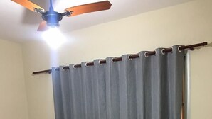 Ein Zimmer mit einem Bett, einem Deckenventilator, einem Fenster mit Vorhängen und einem Fliesenboden.