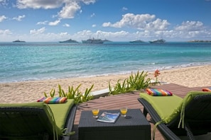 A beachside lounge with two wicker chairs, a wooden table, and a magazine.
