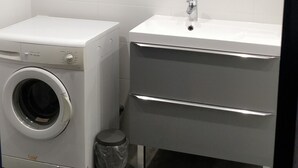 Une petite salle de bain équipée d’un lave-linge, d’un lavabo et d’un miroir.