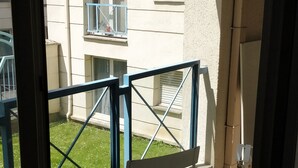 Une vue à travers la fenêtre d’un immeuble doté d’un balcon, d’un étendoir et d’un petit jardin.
