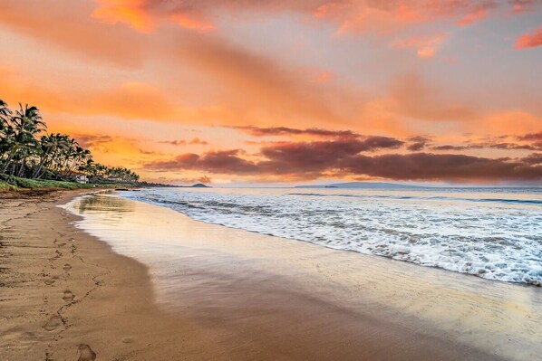 Ein Strand mit Fußspuren, Palmen und einem Sonnenuntergang.