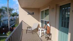 Ein Balkon mit zwei Liegestühlen, einer Holzskulptur und einer türkisblauen Tür.