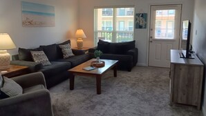 Ein Wohnzimmer mit einer Couch, zwei Sesseln, einem Couchtisch, einer Lampe, einem Deckenventilator und einer Tür mit Fenster.